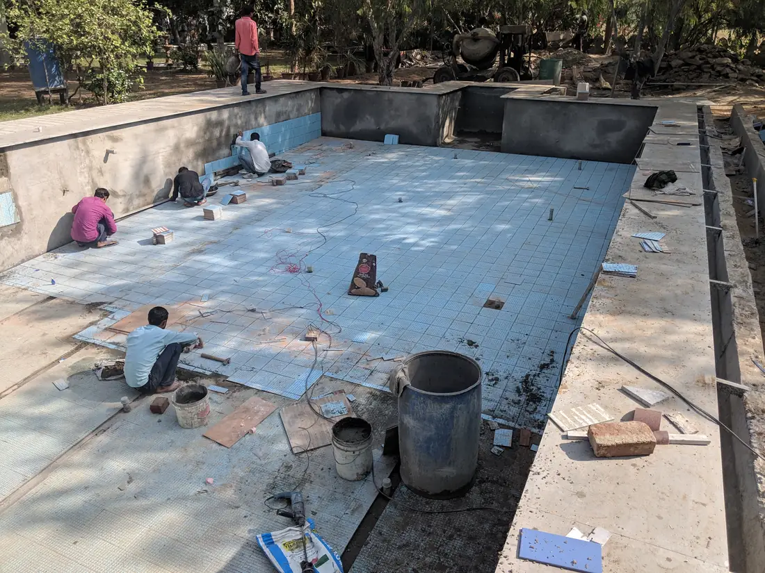 Workers laying tile inside the empty pool shell